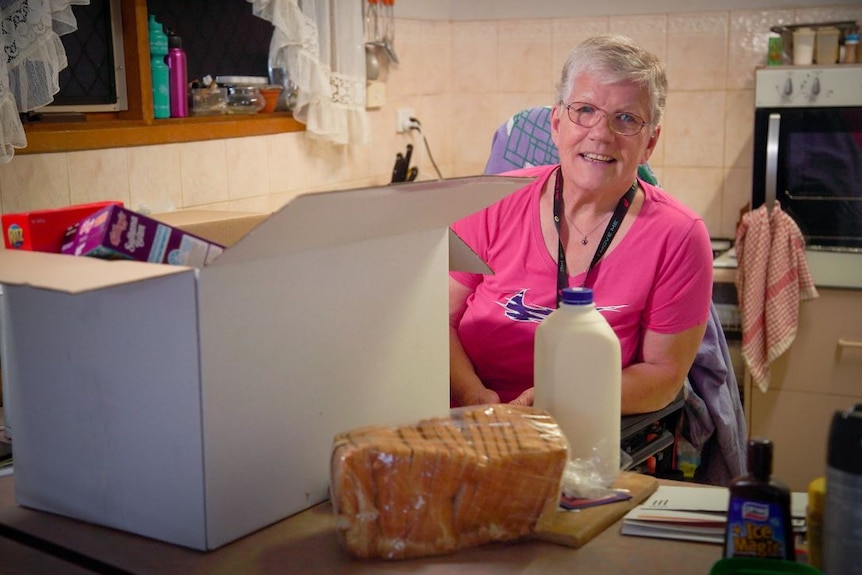 Alice Theunen wearing a pink t-shirt sitting in a chair with a white box placed on a table in front of her