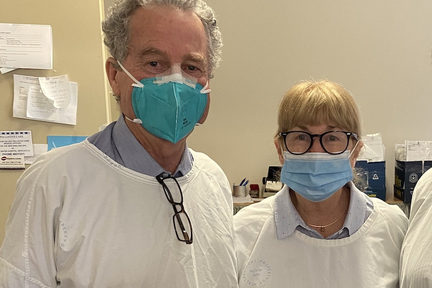 Three people standing in medical gowns and wearing blue face masks