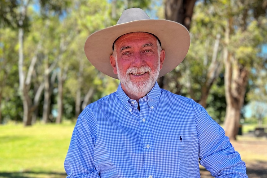 A man with a white beard, wearing a blue shirt and hat, standing outside.