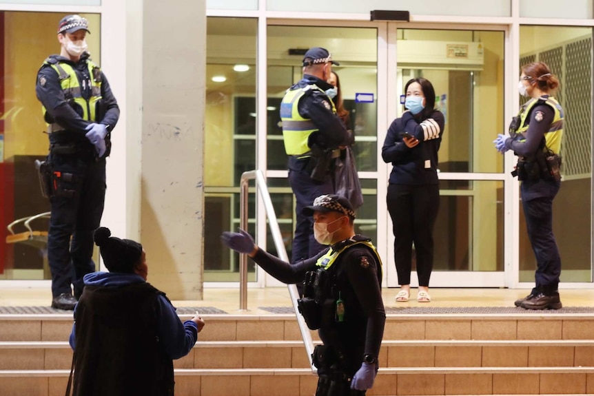 Four police are seen speaking to three people outside a housing tower.