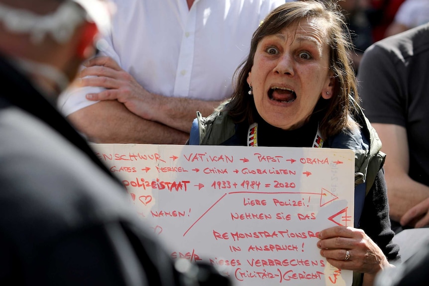 A woman holds a sign up as she shouts while surrounded by other protesters