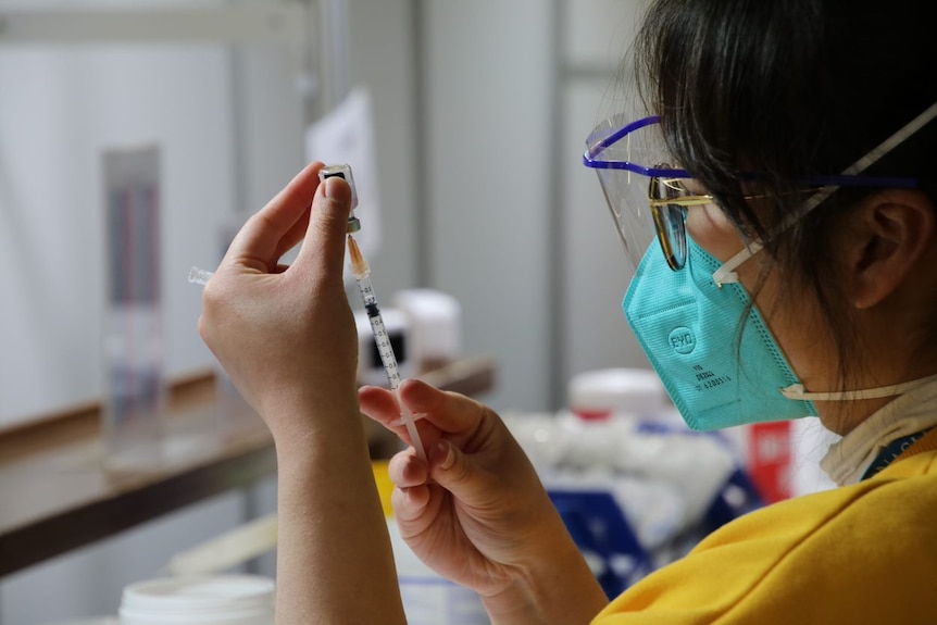 An unidentifiable woman fills a syringe with vaccine.