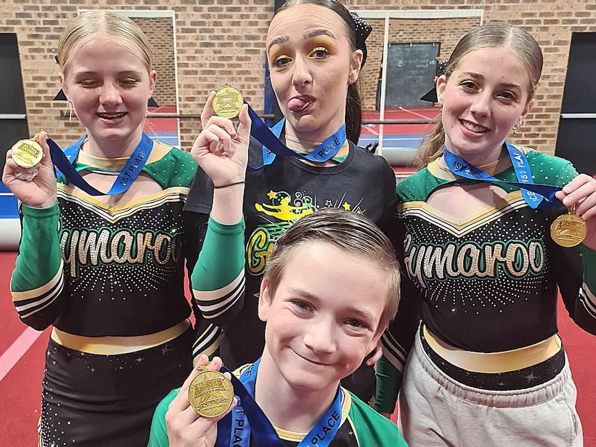 Boy in front and three girls behind in their green and black lycra sports uniform holding up medals smiling