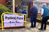 A sign reading polling place, and a line of people coming out of a building