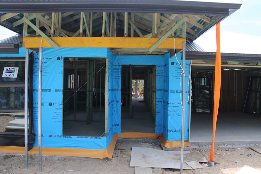 House construction site showing frame and blue plastic on walls at housing estate.