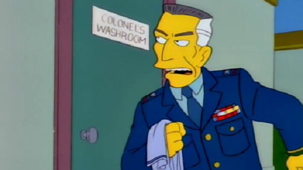 Still from The Simpsons showing a man in a military uniform with a stern expression outside a door that says Colonel's Washroom