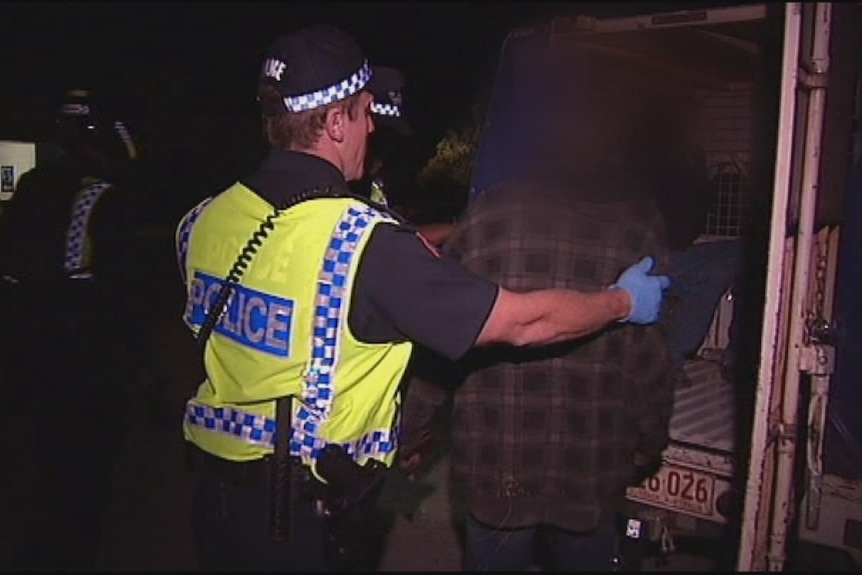 A police officer putting a person into a police van at night.