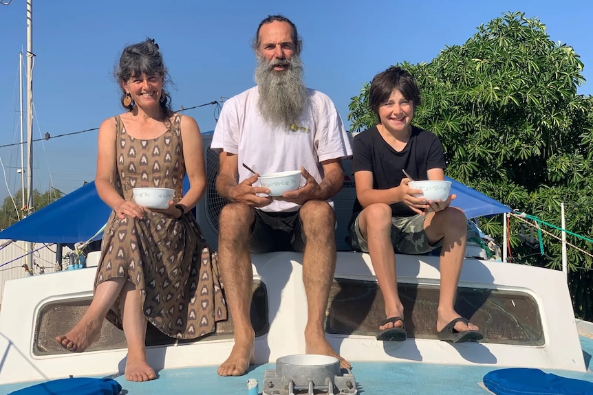 Three people sitting at the top of a boat, holding bowls.