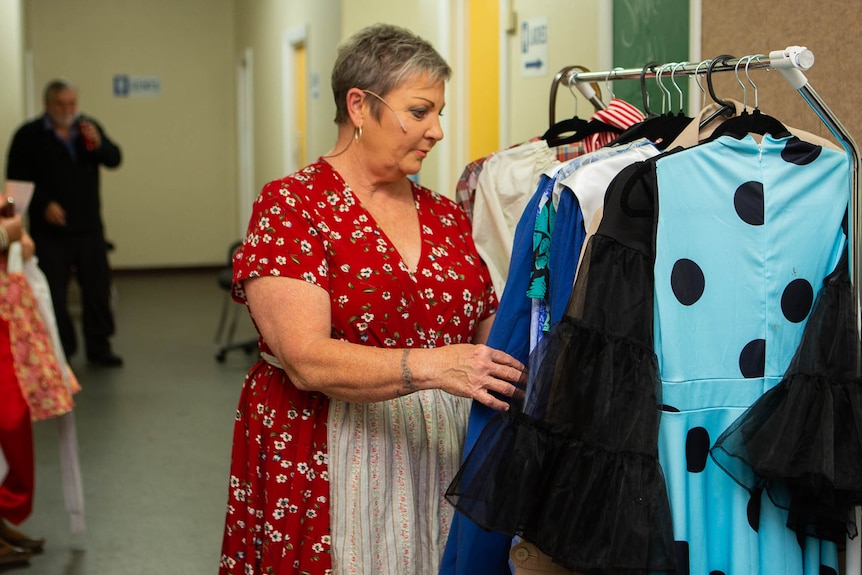 A woman in antiquated dress and apron checking over a rack of costumes backstage.