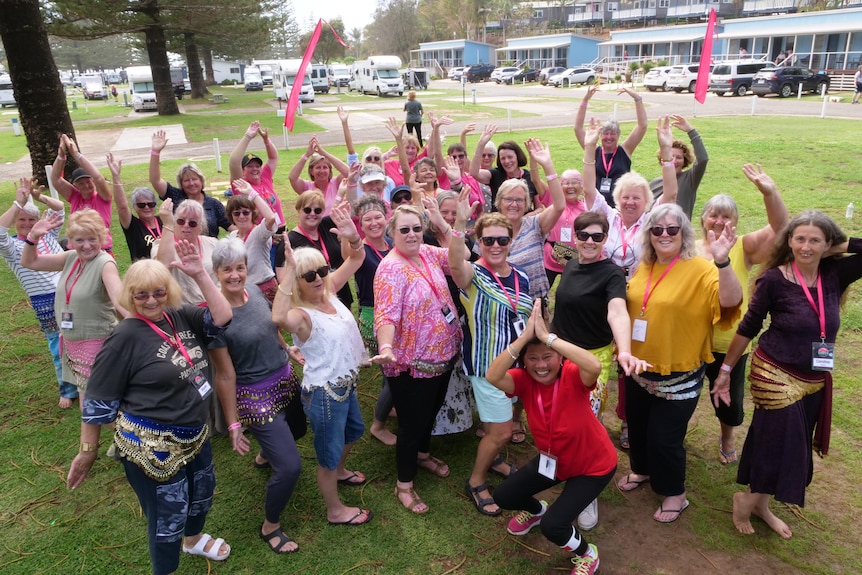 Looking down from above on a group of about 50 women pulling a pose with shimmy belts on and arms up.