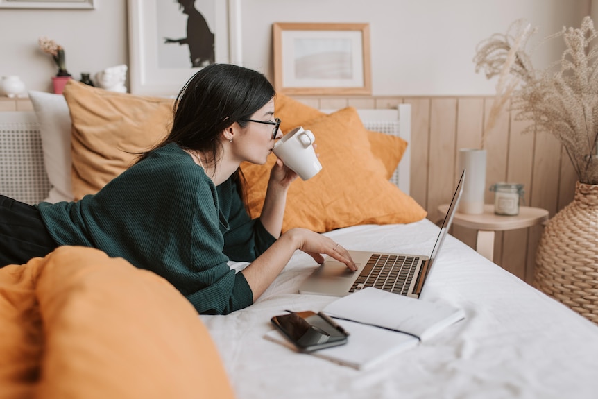 Woman researching on laptop on bed.