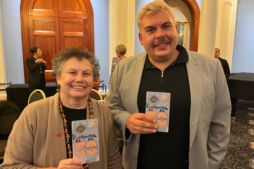 A woman and a man hold up cards containing commemorative coin in a function room