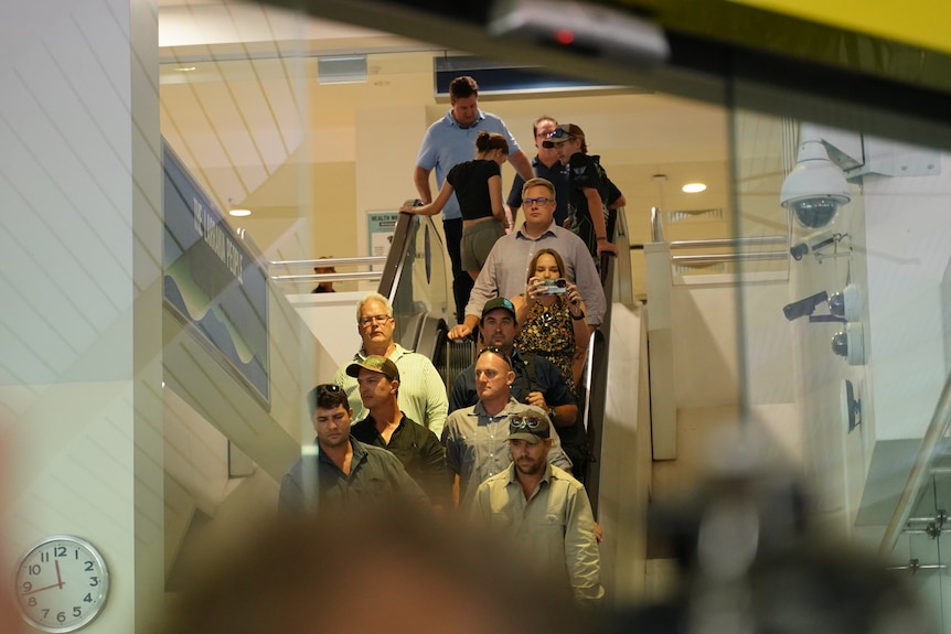 A group of people including celebrity croc wrangler Matt Wright descends an escalator at Darwin Airport.