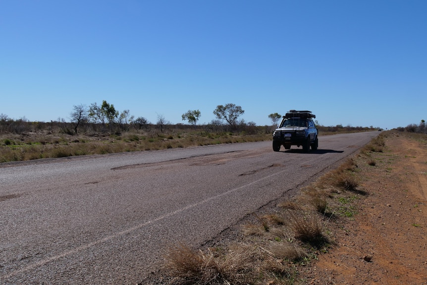 A four wheel drive passes by huge ruptures on a sealed road under a blue outback sky.