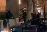 A still from a video shows people in black with faces hidden running down a street and getting into cars.
