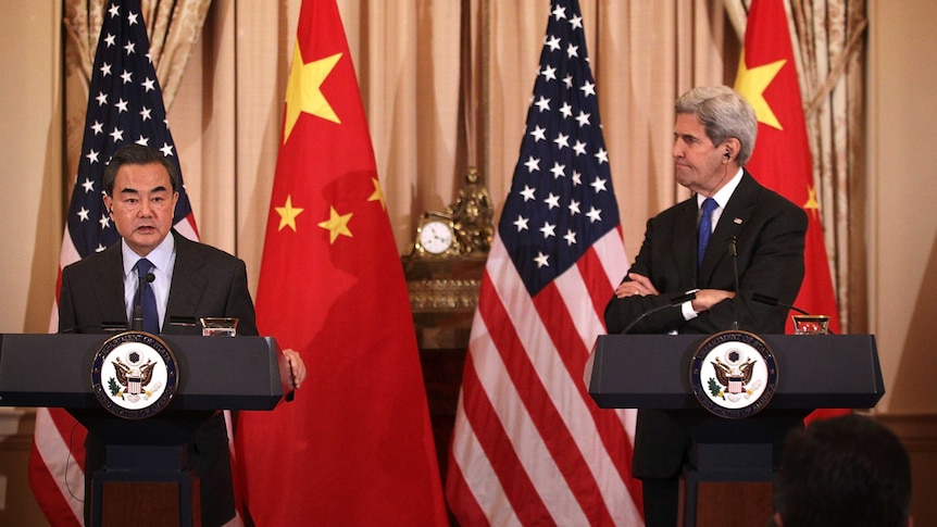 John Kerry watches on with arms folded as Wang Yi speaks at a press conference