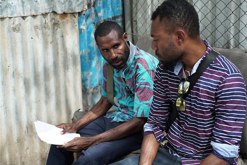 Too men sitting with documents in hand.