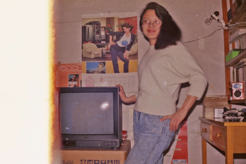 You view a film photograph of a woman posing next to a TV, with its left third distorted due to sun exposure.
