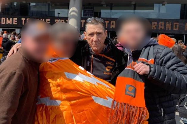 Michael Greene, in a GSW Giants jumper, stands in front of the MCG with friends, who have orange GWS scarves.