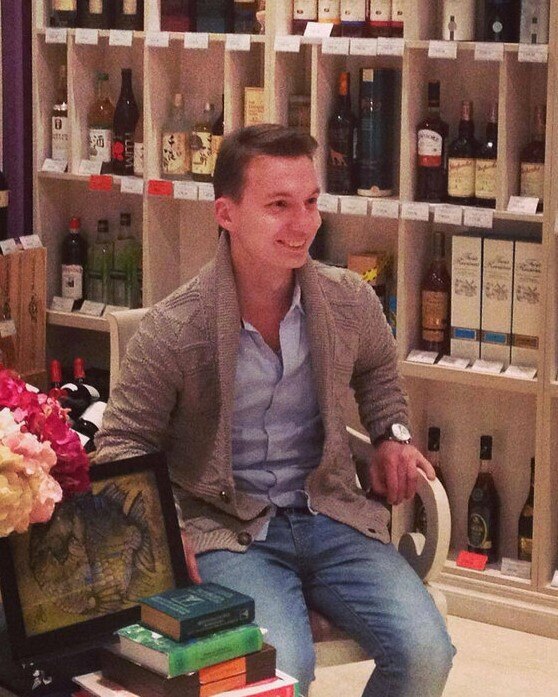 Aleksandr Ermakov sitting in a chair in what appears to be a high-end bottle shop
