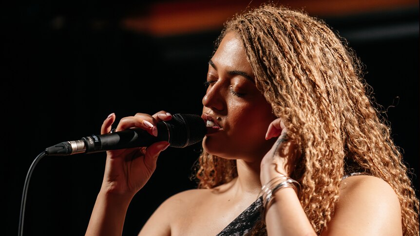 Close up of Mahalia with eyes closed singing into a microphone