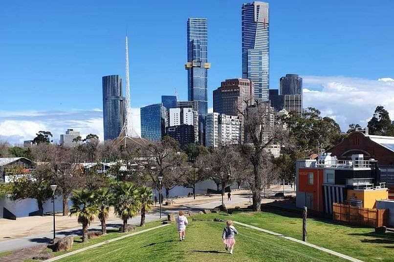 Two small girls running on grass toward city buildings