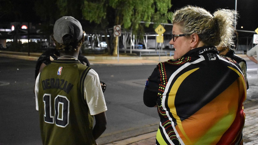 A youth outreach and re-engagement officer and a young boy have their backs to the camera and are talking.