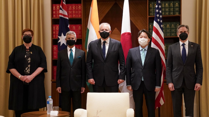 One female and four male politicians stand abreast before the flags of Australia, India, Japan and the US.