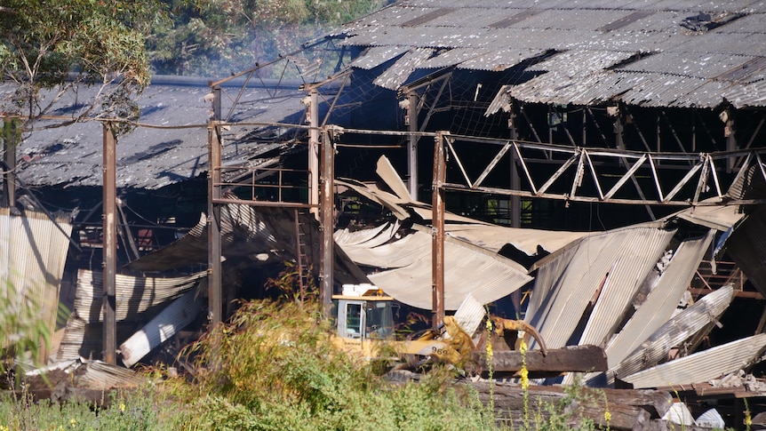 An old burnt down building with smoke still present and some damaged machinery. 