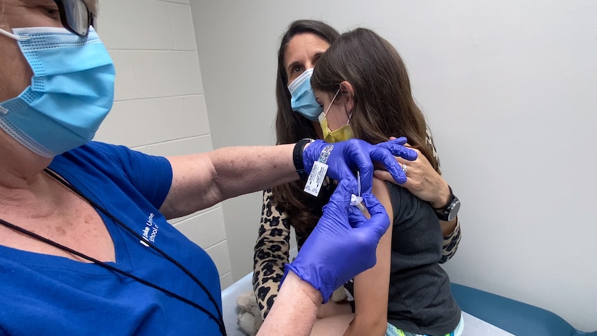 A nine-year-old girl is held by her mother as she gets the second dose of the Pfizer COVID-19 vaccine during a clinical trial.