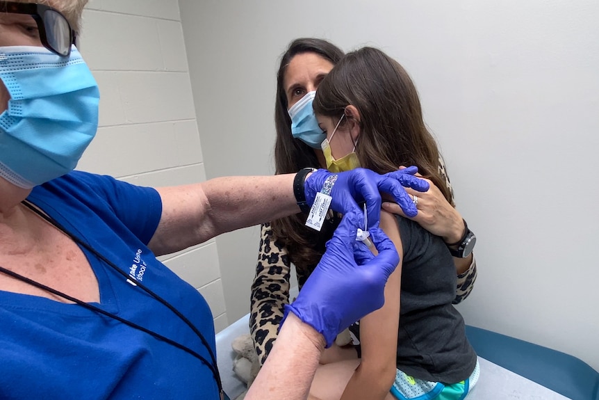 A nine-year-old girl is being held by her mother as she receives the second dose of the Pfizer COVID-19 vaccine during a clinical trial.
