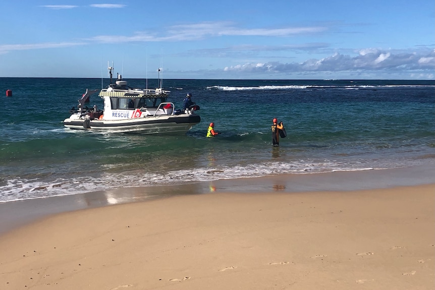 A marine rescue boat waits in the water as crew members assemble on the shoreline