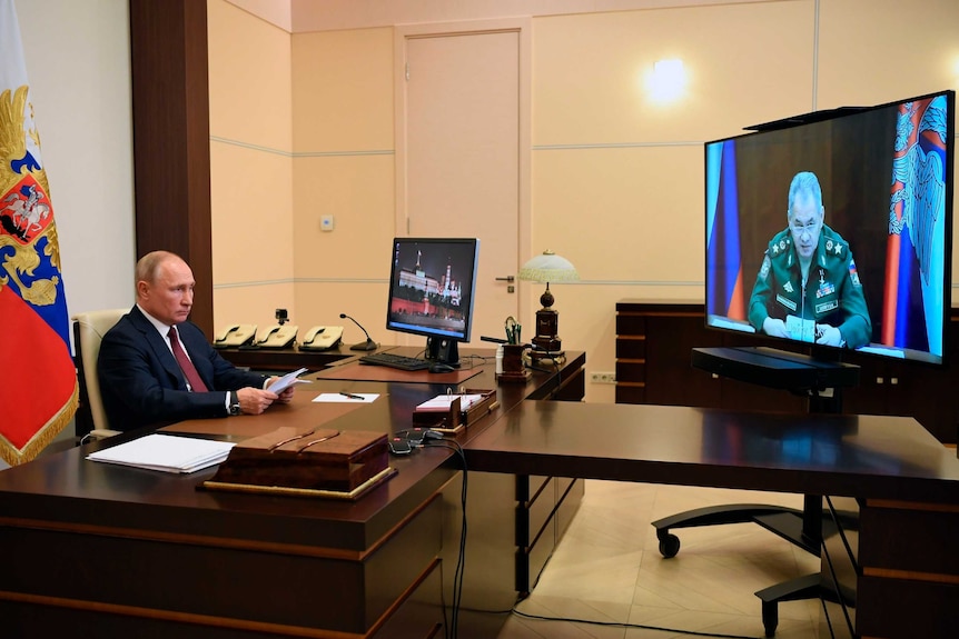 Russian President Vladimir Putin sits at his desk looking at TV screen that shows a video conference with the Defence Minister.