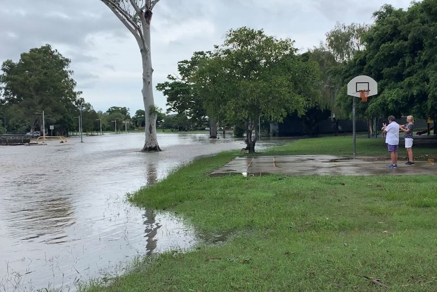 Two people stand on a basketball court looking at a flooded field in a park