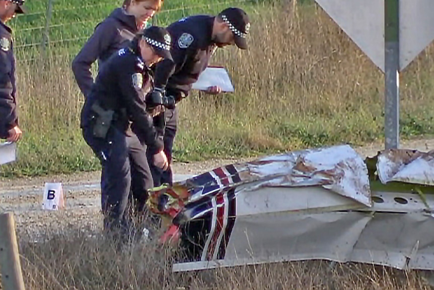 Investigators check the severely damaged nose of the aircraft in a paddock.