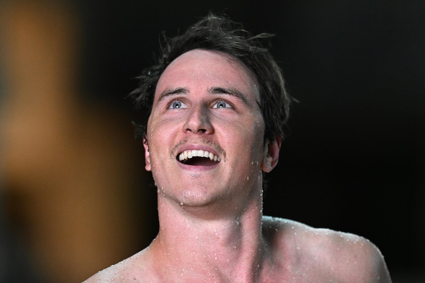 An Australian male swimmer smiles as he looks up into the stands after a race.