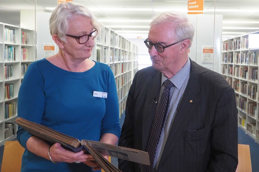 A man and woman standing in a library looking at photo album