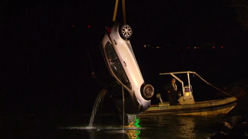 A silver car being hoisted out of a river at night