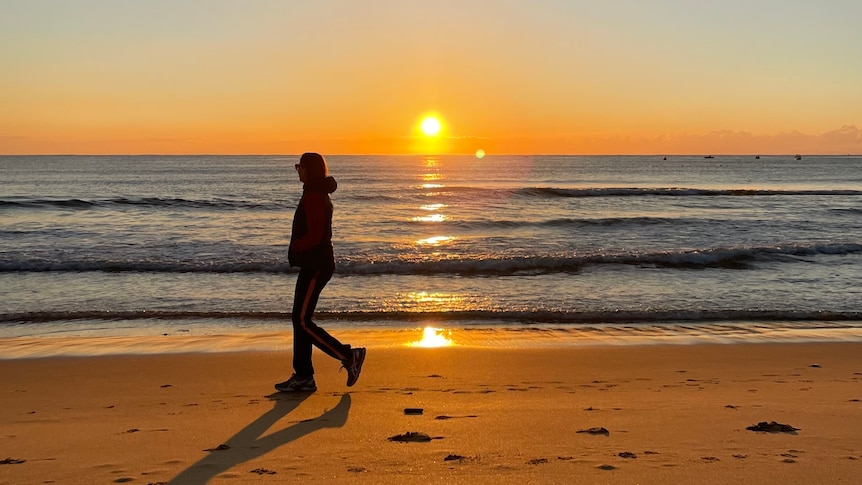 A person walks passed the ocean during sunrise
