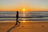 A person walks passed the ocean during sunrise
