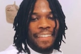 A black man with dreadlocks smiles in a selfie.