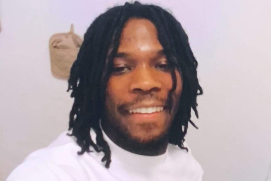 A black man with dreadlocks smiles in a selfie.