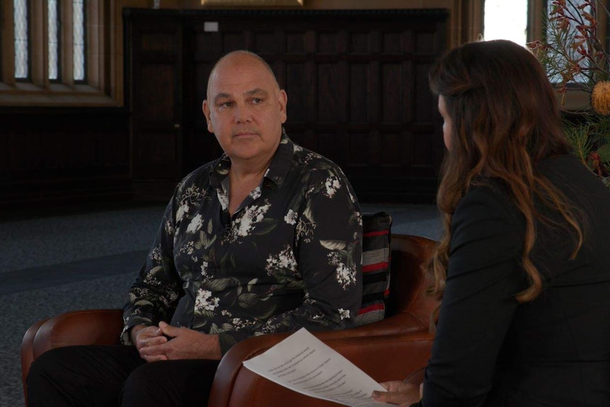 An Indigenous man sits talking to a reporter