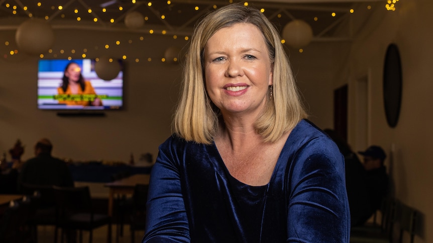 A woman with blonde hair sits in a room with fairy lights.