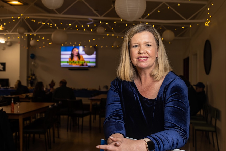 A woman with blonde hair sits in a room with fairy lights.