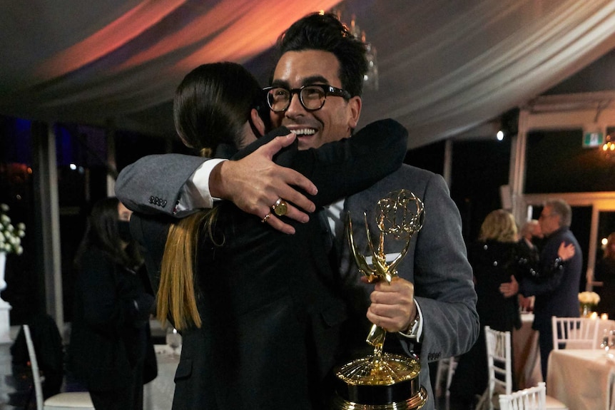 Annie Murphy hugs Dan Levy while he holds an Emmy award.