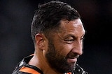 A Wests Tigers NRL player holds the ball as he tries to beat the tackle of a South Sydney opponent.