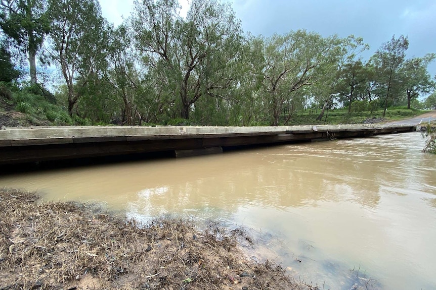 Flood water lies just below the road level of a creek in rural Queensland