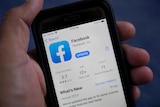 The Facebook app is seen in close-up on a phone being held in a hand