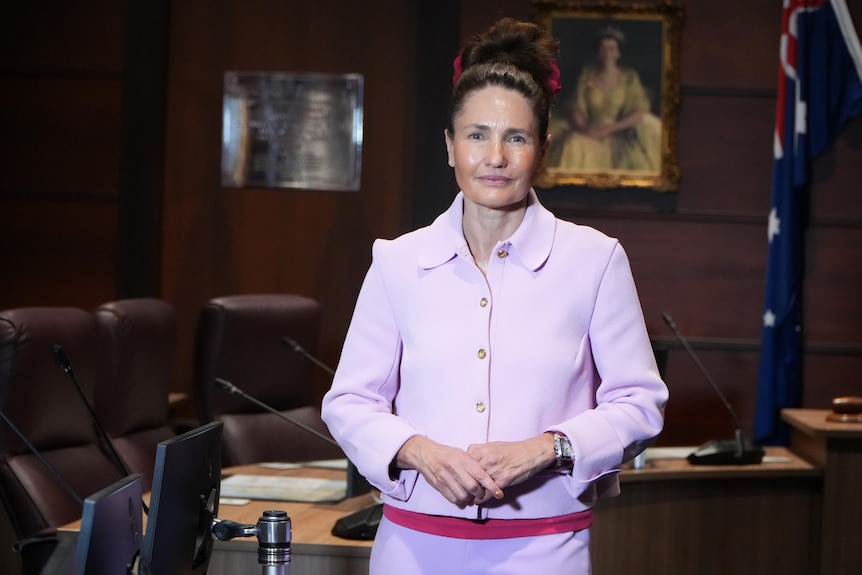 A woman in a powder pink suit stands in a council office